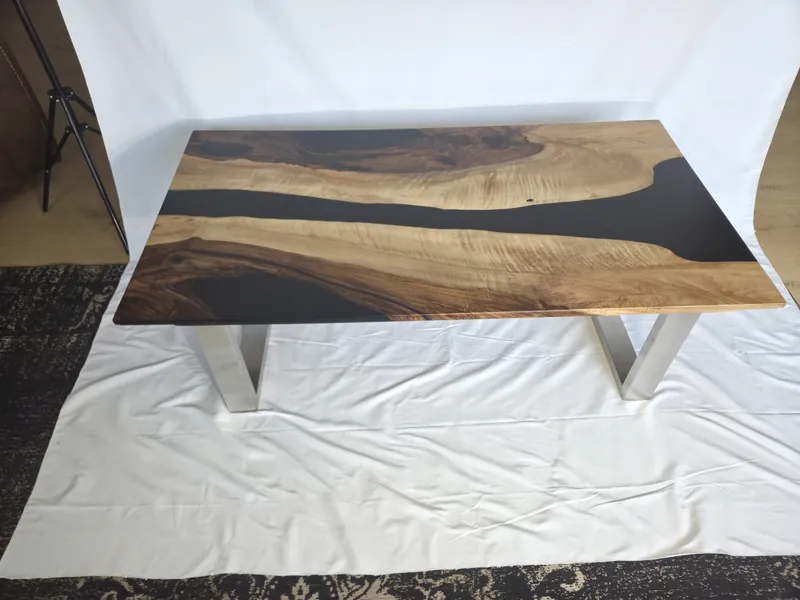 Photo of the finished walnut table with a black epoxy river on steel legs