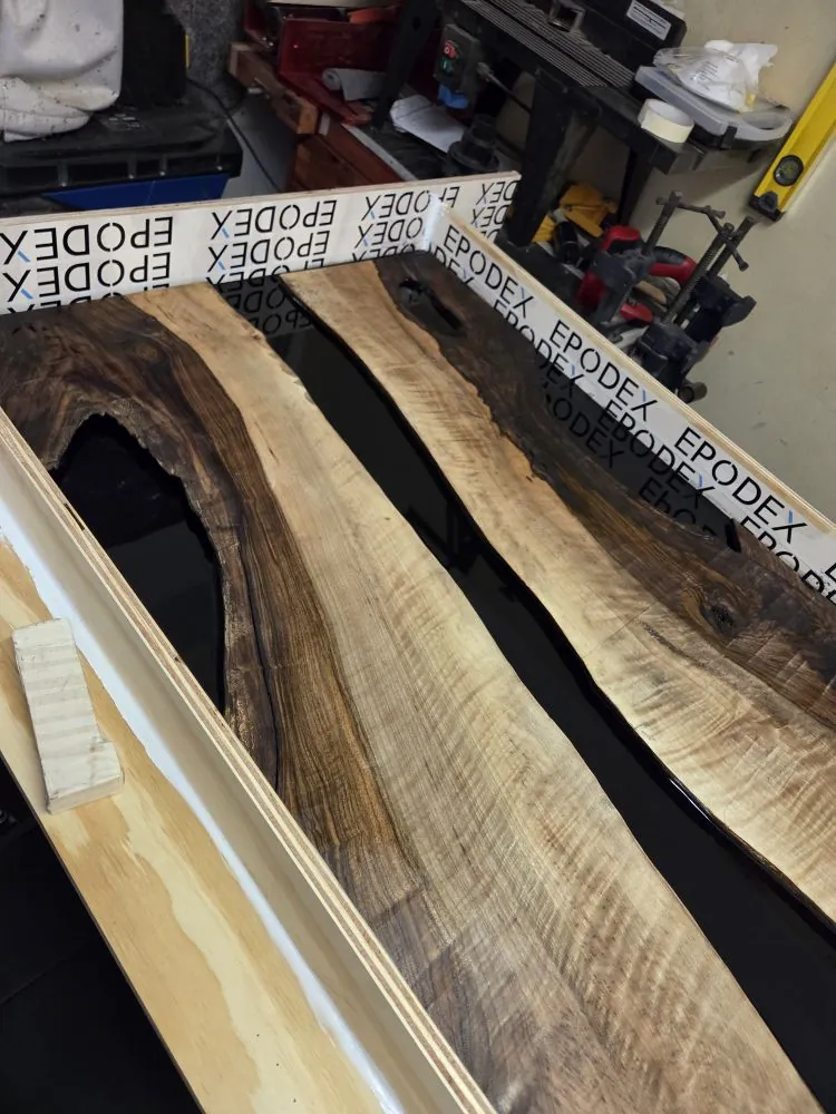 Black epoxy poured between walnut slabs inside a taped mould